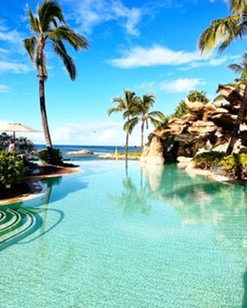 Oceanfront infinity pool overlooking a tropical beach in Hawaii with palm trees and turquoise water.